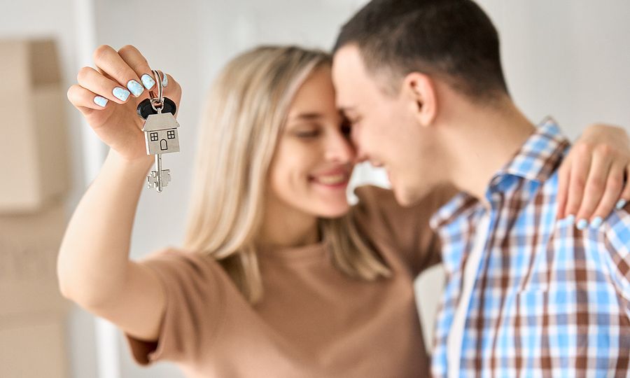 Happy Young Couple Home Owners Holding Keys In New Home. Smiling