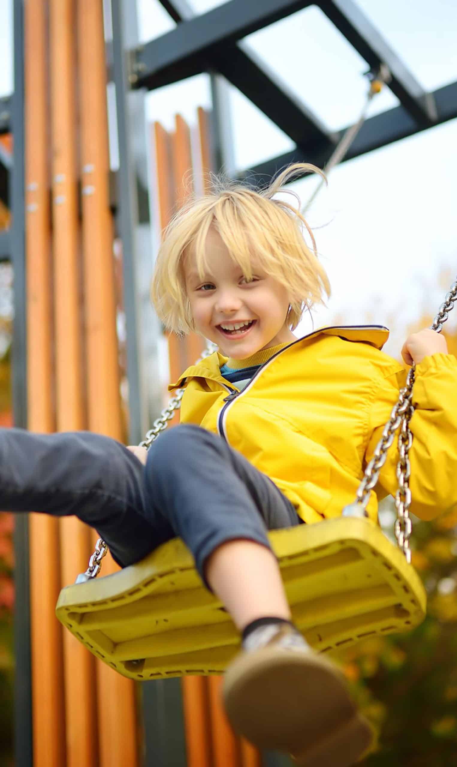 A child playing on a swing in a yellow jacket